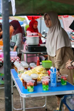 Müslüman bir kadın yerel bir markette taze içecek ve atıştırmalıklarla sokak yemekleri satıyor, Bandung Endonezya, 03 Mart 2025