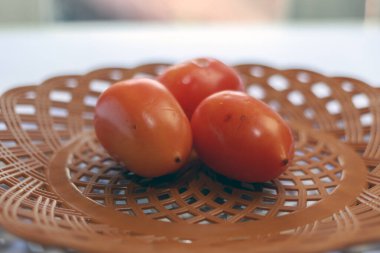 Taze organik domatesler hasır bir tabakta dinleniyor. Yemek fotoğrafçılığı ve mutfak temaları için doğal ve kırsal bir his sunuyor.