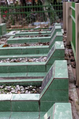 Yeşil mermer mezarlar yeşil çitlerle çevrili huzurlu bir mezarlıkta dizilmiş.