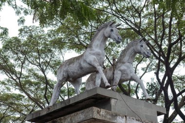 Endonezya, Bandung Endonezya, 04 Mart 2025 'te yemyeşil ağaçlarla çevrili bir anıtın üzerinde duran bir çift yaşlı at heykeli.