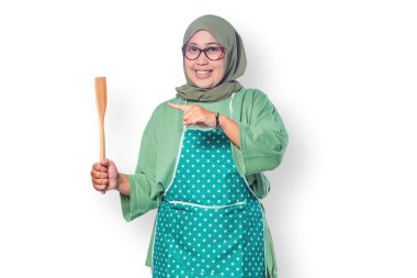 Elinde ahşap bir spatula tutan mutlu Müslüman kadın ev yemeklerini, yemek tutkusunu ve sıcak bir mutfak atmosferini simgeliyor.