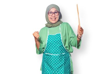 Ahşap bir spatula taşıyan tesettürlü ve önlüklü neşeli Müslüman kadın, yemek pişirme konusunda heyecanlıydı.