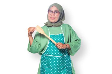 Mutfakta elinde ahşap bir spatula tutan tesettürlü neşeli Müslüman kadın.