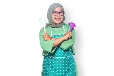 Mutfakta kepçe tutan tesettür ve önlük takan neşeli Müslüman kadın.