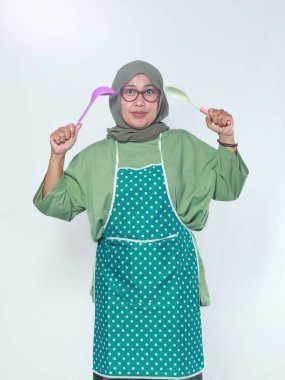 Kıdemli kadın aşçı elinde kepçelerle neşeli bir şekilde yemek pişirme ruhunu gösteriyor.