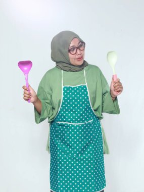 Mutlu kıdemli kadın şef elinde neşeli bir ifadeyle yemek kaşıkları tutuyor.