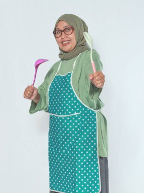 Neşeli bir ifadeyle mutfak gereçlerini tutan mutlu yaşlı kadın.