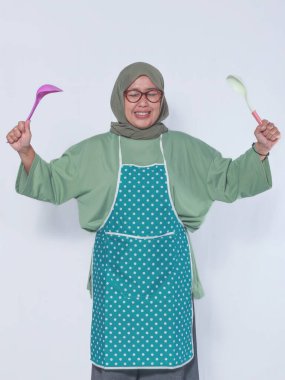 Mutfak gereçleri taşıyan önlük giyen neşeli Müslüman kadın.
