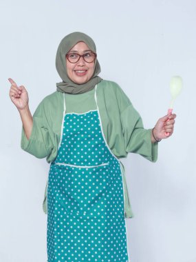 Önlük takan, elinde kepçeyle gülümseyen neşeli bir Müslüman kadın.