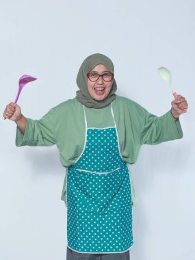 Önlüklü neşeli Müslüman kadın, elinde mutfak gereçleri tutuyordu.