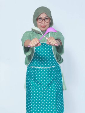 Mutfak kepçeleri taşıyan önlüklü kararlı Müslüman kadın.