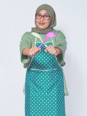 Önlüklü neşeli Müslüman kadın elinde neşeyle yemek pişirme aletleri tutuyor.