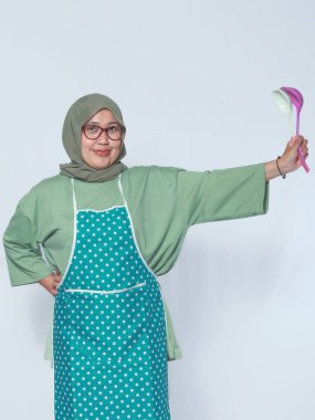 Önlüklü, elinde kepçeyle yemek pişirmeye hazır Müslüman bir kadın.