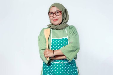 Kendine güvenen Müslüman kadın şef elinde tahta bir kaşıkla ev yemeklerini, restoran işlerini ve aşçılık tutkusunu simgeliyor.