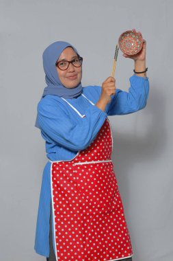 Müslüman kadın yemek pişirirken, yemek çubukları tutarken ve dekoratif bir kase tutarken gülümsüyor.