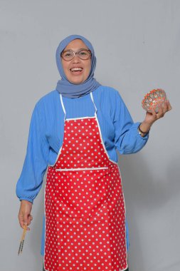 Mutfakta elinde dekoratif bir kâse ve yemek çubuğu tutan neşeli Müslüman kadın.