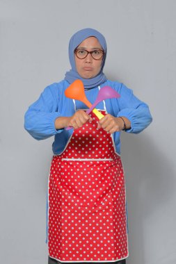 Hüsrana uğramış Müslüman kadın önlük ve tesettüre bürünmüş, elinde hayal kırıklığına uğramış bir ifadeyle mutfak gereçleri tutuyor. Yemek pişirme ve mutfak temaları için mükemmel