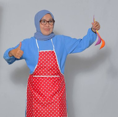 Kendine güveni tam Müslüman bir kadın mutfak gereçleri tutuyor ve baş parmağını kaldırıyor.