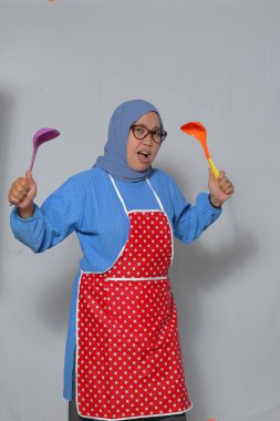 Komik Müslüman kadın, elinde mutfak aletleri tutarak ifade edici bir ifade takınıyor.