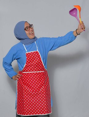 Mutluluk ve neşe dolu mutfak gereçleri taşıyan mutlu Müslüman kadın.