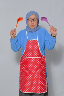 Hüsrana uğramış Müslüman kadın önlük giyiyor, mutfak gereçlerini tutuyor, evde yemek pişirirken stres yapıyor.