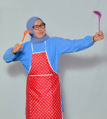 Komik aşçı kepçe tutarak neşeli bir yemek pozu veriyor, mutfakta neşeli davranıyor.