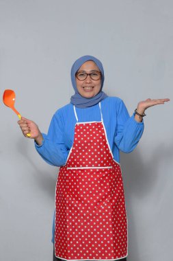 Kıdemli kadın şef elinde kepçeyle gülümseyerek yemek yapmaya hazır.