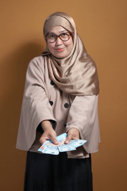 Endonezya Rupiası sunan tesettürlü Müslüman bir kadın cömertliği, finansmanı ve iş fırsatlarını simgeliyor