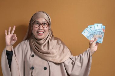 Endonezya parası elinde tutan mutlu Müslüman kadın, finansal başarı ve refahı simgeliyor.