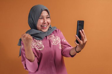 Müslüman kadın video çekiyor ve başarıyı mutlu bir gülümsemeyle kutluyor, modern yaşam tarzında heyecan ve neşe gösteriyor.