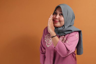 Müslüman bir kadın şakacı bir ifade ve eğlenceli bir gülümseme ile gizlice fısıldıyor.