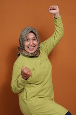 Mutlu, kendine güvenen bir kadın başarıyı kollarını kaldırarak ve neşeli bir gülümsemeyle kutluyor. Güçlendirme, motivasyon ve duygusal ifade temaları için mükemmel.