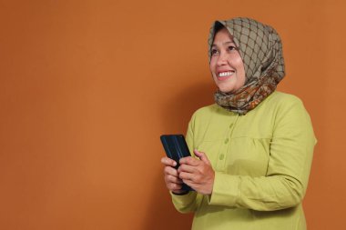 Mutlu Müslüman kadın kapalı mekanda neşeli bir ifadeyle akıllı telefon kullanıyor. Teknolojik yaşam tarzı, sosyal medya pazarlaması ve mobil iletişim temaları için harika.