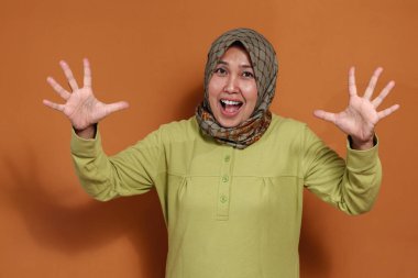 Heyecanlı Müslüman kadın neşeli bir ifade ve sürprizle el kaldırıyor.