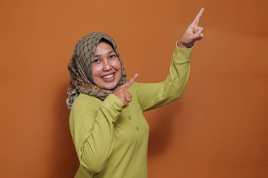 Neşeli Müslüman kadın heyecanla ve mutlu bir ifadeyle işaret ediyor.