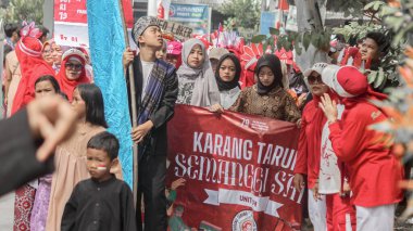 Geleneksel ve modern kıyafetler giyen bir grup insan Bağımsızlık Günü geçit töreninde bir pankart taşıyor ve birlik kutluyorlar. Bandung - Endonezya, 17 Ağustos 2024