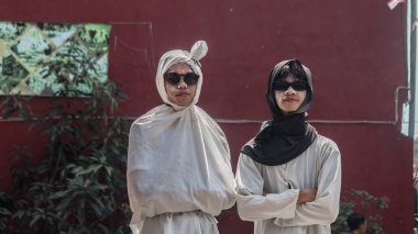 Güneş gözlüklü ve boyalı yüzlü eşsiz beyaz kostümler giymiş iki genç adam, açık hava etkinliğinde güvenle ayakta duruyorlar. Bandung - Endonezya, 17 Ağustos 2024