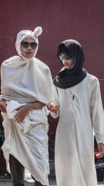Hayaletli bir Pocong gibi giyinmiş bir adam ve tesettürlü bir kadın gün ışığında birlikte yürüyüp eşsiz bir kültürel sahne yaratıyorlar. Bandung - Endonezya, 17 Ağustos 2024