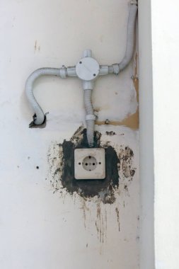 Eski duvar elektrik prizinde görünür toprak ve açık kablolar var. İhmal edilmiş elektrik altyapısı, bozulma veya bakım sorunlarını göstermek için mükemmel.