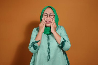 Stresli bir kadın duygusal ifadeyle yüzüne dokunuyor. Bitkinlik, endişe, yorgunluk ya da otantik duygularla baş ağrısı gösteriyor.