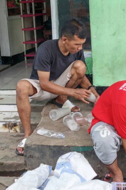 Bandung, Endonezya 29 Nisan 2025, adam dışarıda oturuyor kaldırımda plastik bardakları sınıflandırıyor.