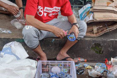 Bandung, Endonezya 29 Nisan 2025, Adam kaldırımda makasla geri dönüşüm için plastik ambalaj kesiyor
