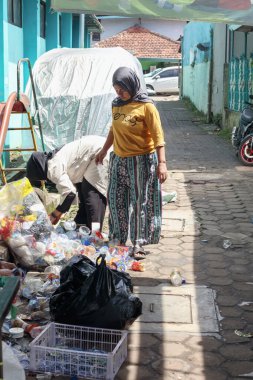 Bandung, Endonezya 29 Nisan 2025, iki kadın dar sokaktaki parlak binaların yakınındaki plastik atığı yönetiyor ve sıralıyor