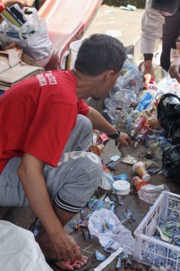 Bandung, Endonezya 29 Nisan 2025, Toplum temizliği sırasında yerde çömelmiş ve karışık plastik atıklarını sınıflandıran adam.