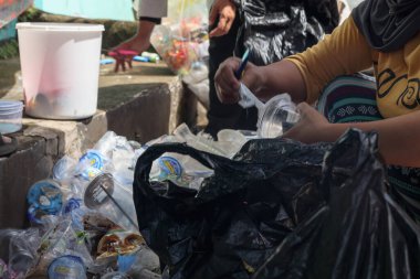 Bandung, Endonezya 29 Nisan 2025. Plastik bardaklardan etiketleri söken ve çöpleri geri dönüşüm için ayıran kadının elleri.