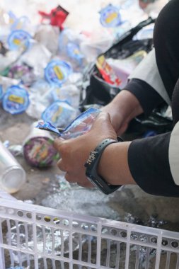 Bandung, Endonezya 29 Nisan 2025, Eller geri dönüşüm için atılan konteynırlar arasında plastik şişe etiketi kesiyor