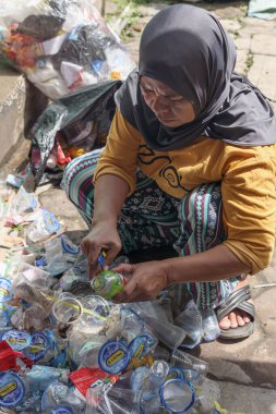 Bandung, Endonezya 29 Nisan 2025, Plastik atık yığınları arasında yeşil şişe kesen kadın