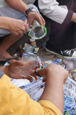 Bandung, Endonezya 29 Nisan 2025, Eller plastik geri dönüşüm halkalarıyla dolu beyaz sandığın üzerinde plastik bardak kenarı kesiyor.