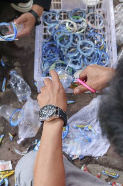 Bandung, Endonezya 29 Nisan 2025, plastik halkalarla dolu sepetin yanında plastik şişeyi kesen ellere yaklaş.