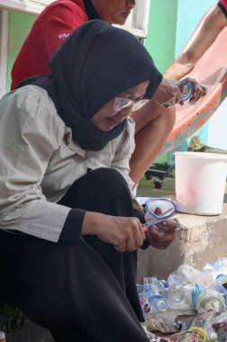 Bandung, Endonezya 29 Nisan 2025, Geri dönüşüm sırasında plastik bardağı makasla kesen kadın.